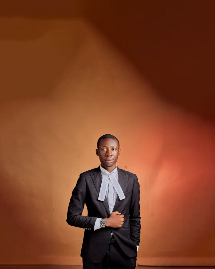 Young lawyer poses confidently in a suit against a warm backdrop.